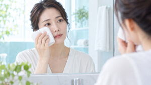 女性が鏡を見ながら目の下に冷たいタオルをそっと当てている様子