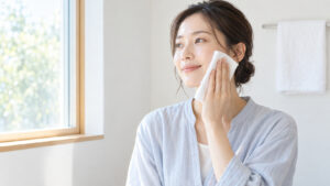 女性が朝の明るい洗面所で柔らかな白いシートを頬にそっと押し当てている様子