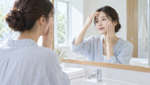 女性が朝の洗面所で鏡を見ながら額と頬の肌状態をそっと確認している様子